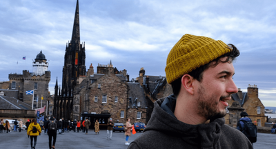 Jack wearing a mustard beanie on Edinburgh’s Royal Mile, with historic buildings behind him.
