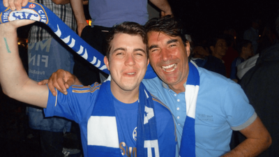 Jack and his dad smiling with their arms around each other, wearing blue Chelsea scarves.
